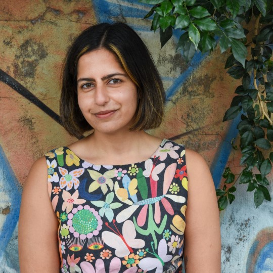 Young woman standing against a brick wall with a small leaved branch with brown short hair and a floral top